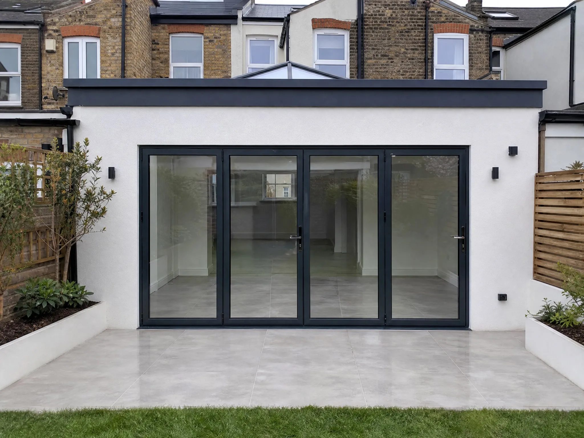 Single-storey rear extension with white render, a roof lantern and dark aluminium bifold doors onto a porcelain patio